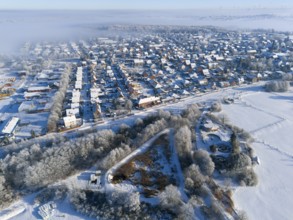 Aerial view of snowy city with fog and frost-covered fields, trees and buildings, aerial view,