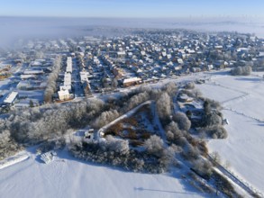 Snowy city landscape from the air with frost-covered houses and fields under blue sky, aerial view,
