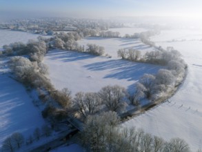 Winter landscape with snowy fields and trees, city skyline in the background under blue sky, Fuhse