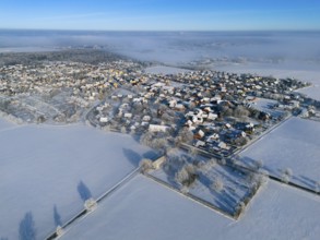 Snowy village nestled in white fields under a clear sky from a bird's eye view, aerial view, partly
