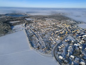 Wintery village landscape in foggy surroundings with snowy forests and fields, aerial view, partly