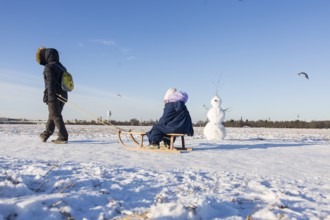 A woman drags a child on a sled past a snowman on Tempelhofer Feld in Berlin on 11.01.2026