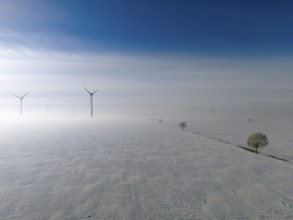Wide snow-covered plain with wind turbines in fog under blue sky, aerial view, wind turbine and