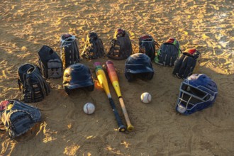 Baseball gear bats, mitts, helmets and a catchers mask laid on sandy field, ready for practice or