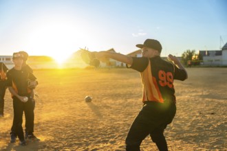 Young baseball player throwing a pitch with a glove during practice, with other players waiting on