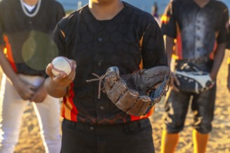 Young baseball player standing on a dusty field, holding a baseball in one hand and a catcher's