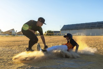 Two young baseball players engaged in a competitive game, one player sliding into base creating a