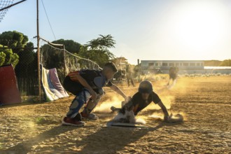 Young baseball player sliding into base on dusty infield as catcher reaches to tag him, dynamic