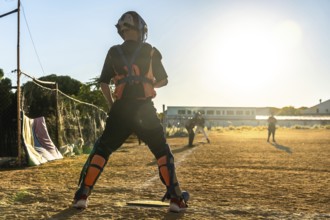 Catcher in full gear stands on a dusty baseball field at sunset, silhouetted against golden light