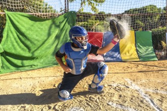 Boy catcher wearing helmet, chest protector, and leg guards, catching a baseball with glove,