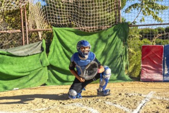 Youth baseball player wearing catcher's helmet and protective equipment, ready to catch at home