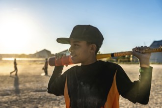 Young male baseball player holding a bat over his shoulder, wearing a cap and jersey, standing on a