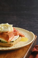 A plate holds a piece of toast topped with salmon, cream, and herbs. The setting appears casual and
