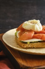 Close-up view of toasted bread with layers of avocado, smoked salmon, cheese and a poached egg on