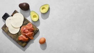 Smoked salmon, slices of goat cheese, halved avocados, and an egg on a wooden cutting board.