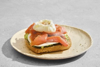 Toasted bread with smoked salmon, avocado, goat cheese and a poached egg on top. The food is