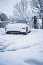 A modern electric car is parked in a snowy area next to a charging station, Tesla Model Y electric