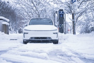An electric car is parked in a snowy winter landscape next to a charging station, Tesla Model Y