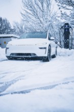 White electric car in a snowy landscape next to a charging station, Tesla Model Y electric car,