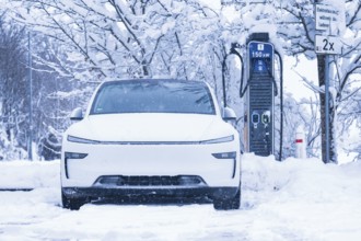 An electric car parked in the snow, close-up of the charging station in the background, Tesla Model