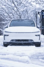 A futuristic white electric car stands in the snow in front of a charging station, Tesla Model Y