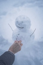 A hand shapes a small snowman in the snow, simple winter joy, Waldachtal, Freudenstadt district,