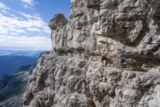 Two mountaineers on an exposed rock band in the secured via ferrata Bocciere Centrale, Brenta