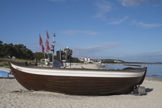 Boat with fishing flags is lying on a sandy beach, behind the spa hotel, blue sky, Binz, seaside