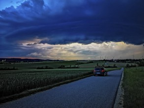 Supercell, car driving on a small road towards an approaching thunderstorm, impressive and