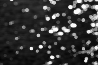 Abstract black background, sparkling white lights, bokeh balls, light reflections on water surface,