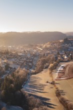 Aerial view of a snowy village at sunrise with snow-covered trees and hills in the background,