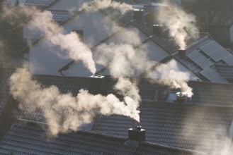Smoking chimneys over roofs in a winter atmosphere illuminated by sunrays, symbolic image,