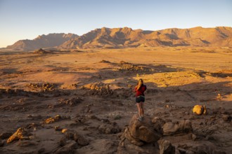 Young woman standing in desert landscape with Brandberg in morning light, at sunrise, Erongo,