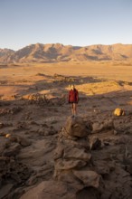 Young woman standing in desert landscape with Brandberg in morning light, at sunrise, Erongo,