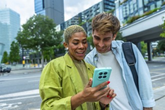 Business colleagues standing outdoors in a city, happily sharing and viewing content together on a