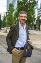 Confident mature businessman with beard and suit jacket smiling at camera, holding a messenger bag