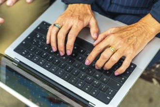 Mature womans hands with painted nails and rings typing on a laptop keyboard, close up conveying