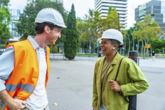 Two diverse construction professionals wearing hard hats and safety gear, happily collaborating and