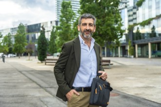 Confident mature businessman carrying a briefcase and smiling at the camera, standing outdoors with