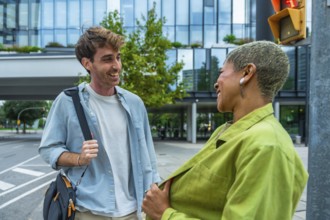 Two diverse business colleagues laugh and chat while walking on a city street, sharing a friendly,