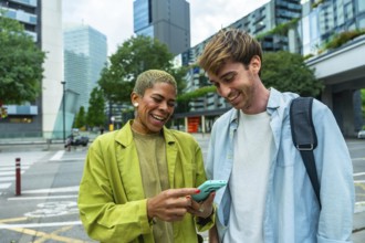 Diverse colleagues standing outdoors, laughing happily while looking at a smartphone, sharing a