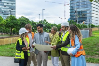 Group of multi ethnic architects, engineers, and executives reviewing blueprints and discussing