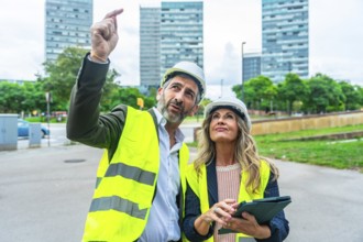 Male and female architects or engineers wearing hard hats and high visibility vests inspecting a