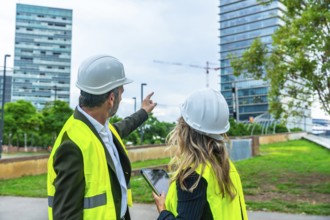 Architects and engineers wearing hard hats and safety vests discussing city development while