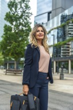 Confident businesswoman wearing a pinstripe suit, holding a briefcase and looking forward, standing