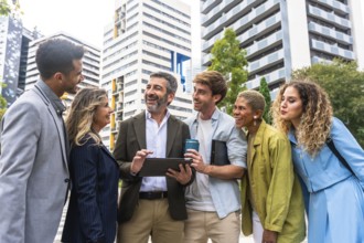Diverse business professionals working together laughing outdoors, analyzing a digital tablet,