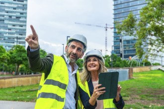 Architects and engineers review development plans on a tablet while pointing toward a construction