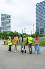 Group of executives and architects wearing safety vests and hard hats, observing a construction
