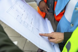 Engineers and architects in safety vests analyzing and discussing a detailed building blueprint,