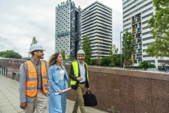 Diverse team of engineers and executives wearing safety vests and hard hats walking outdoors in a